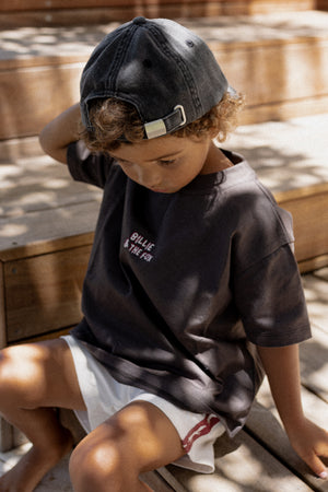 Child wearing a dark t-shirt and cap sitting on a wooden surface.