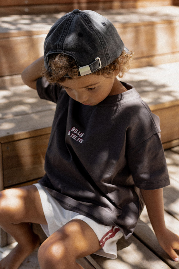 Child wearing a dark t-shirt and cap sitting on a wooden surface.